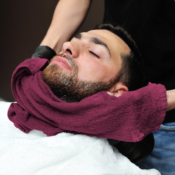 Barber dries customer's beard with burgundy salon towel