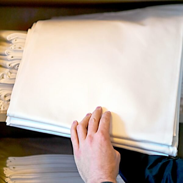 Person grabbing folded white linen sheet from closet