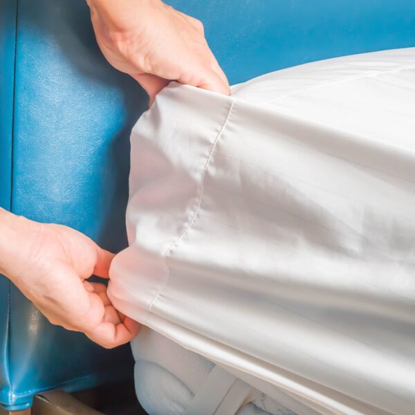 Person inserting white linen fitted sheet cover over mattress