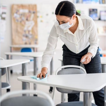 Teacher wearing PPE mask wiping down student table