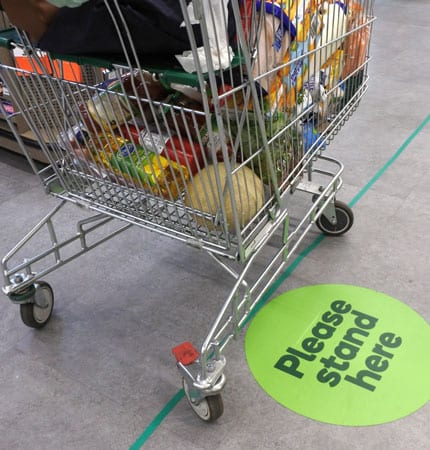 Shopping cart standing by the Please Stand Here sticker at grocery store during COVID