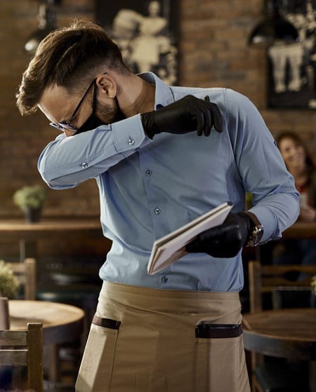 Waiter wearing mask coughing into his elbow