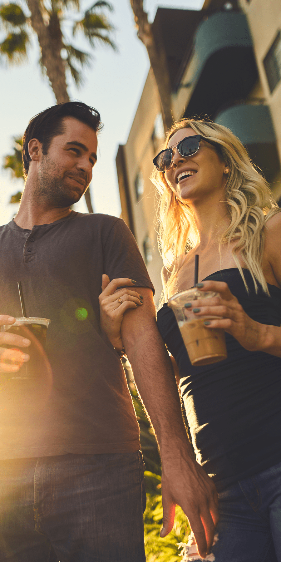 Couple holding iced beverages walking arms linked around the city