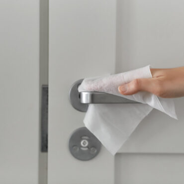 Closeup of a woman's hand cleaning an office door handle with a wet wipe.